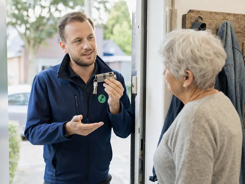 Slotenmaker laat een oudere bewoonster een nieuwe veiligheidscilinder met sleutels zien